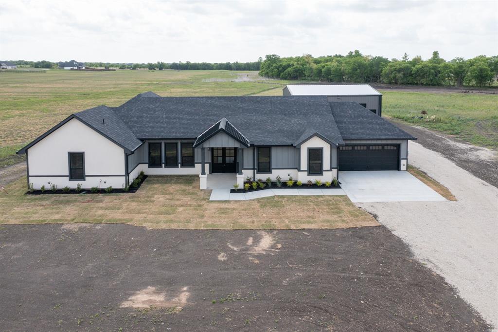 901 Old Maypearl Road Waxahachie, TX 75167 - Photo 2 of 17 The property features a dark gray shingled roof, a light-colored exterior with dark trim, a two-car garage, and a concrete driveway