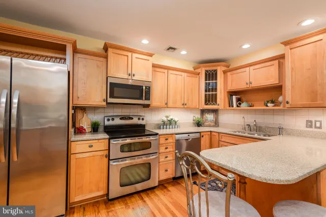 a kitchen with stainless steel appliances granite countertop a sink a stove a refrigerator cabinets and a dining table with wooden floor