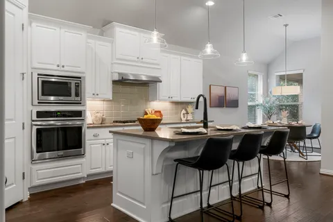 a kitchen with stainless steel appliances kitchen island granite countertop a stove top oven a sink dishwasher and white cabinets with wooden floor