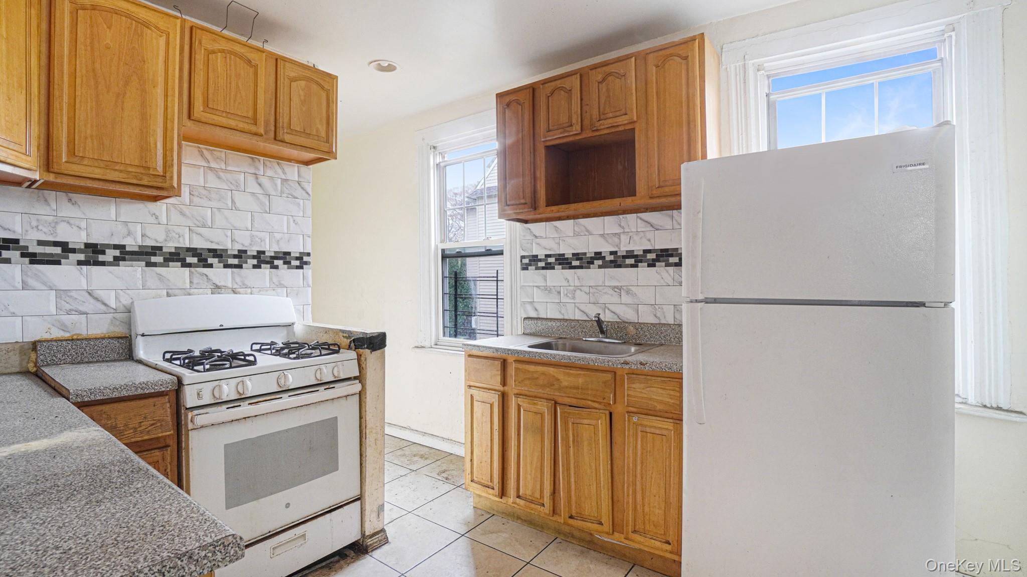 111 South Fulton Avenue Mount Vernon, NY 10550 - Photo 11 of 19 Kitchen with white appliances, brown cabinetry, tasteful backsplash, light tile patterned floors, and light countertops