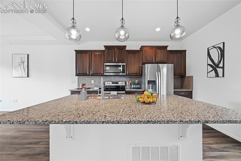 9414 Timberlake Loop Colorado Springs, CO 80927 - Photo 13 of 40 Kitchen with a breakfast bar area, dark wood finish cabinets, stainless steel appliances, decorative backsplash, and light stone counters