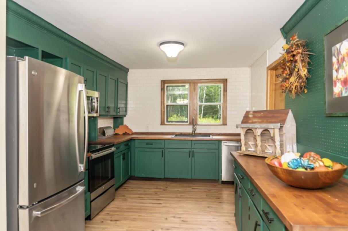 126 Jay Cooke Road Esko, MN 55733 - Photo 6 of 19 Kitchen featuring green cabinetry, wooden counters, stainless steel appliances, light wood finished floors, and decorative backsplash