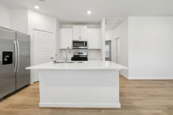 a kitchen with stainless steel appliances a refrigerator a stove a sink and white cabinets