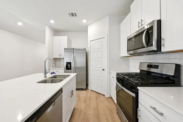 a kitchen with stainless steel appliances a sink a stove a microwave a refrigerator a sink and cabinets