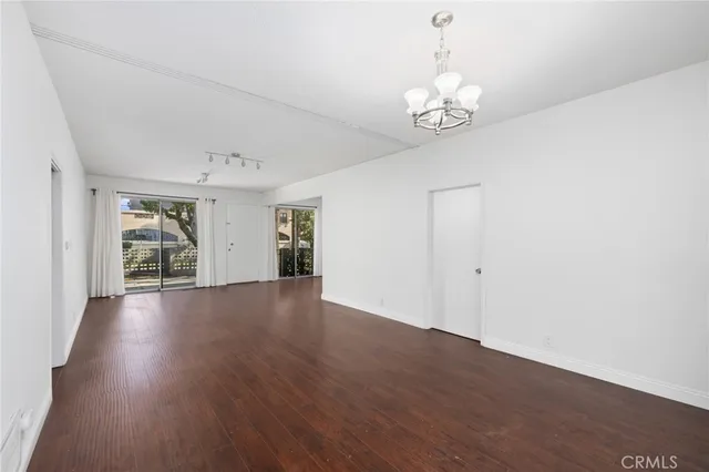 an empty room with wooden floor chandelier and windows