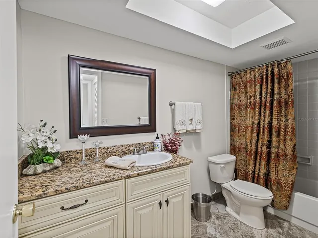 a bathroom with a granite countertop sink a toilet a mirror and shower curtain