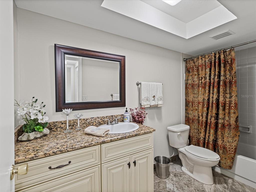 9615 Midiron Court, Unit 9615 New Port Richey, FL 34655 - Photo 22 of 36 a bathroom with a granite countertop sink a toilet a mirror and shower curtain