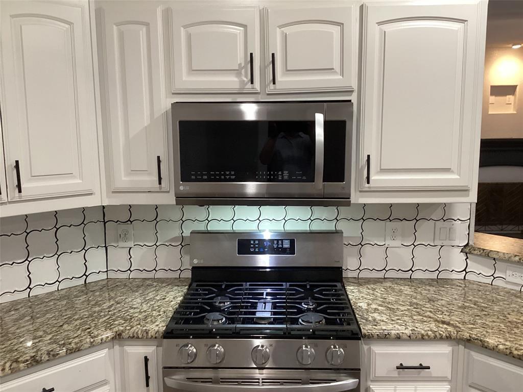 10320 Point Lobos Trail Fort Worth, TX 76177 - Photo 5 of 33 Kitchen featuring white paneled cabinetry with black hardware, stainless steel gas range, over-range microwave, granite countertops, and a decorative tile backsplash