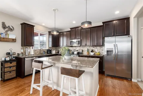 a kitchen with granite countertop a center island a refrigerator cabinets wooden floor and a chandelier