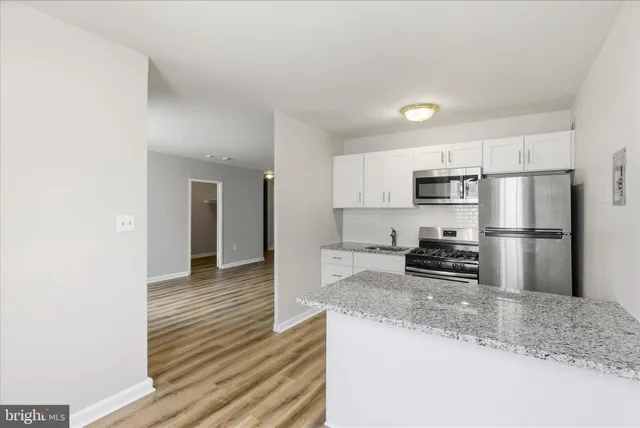 a kitchen with stainless steel appliances granite countertop a refrigerator a stove a sink and white cabinets with wooden floor