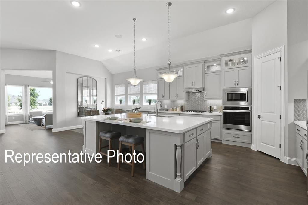 331 Fire Blade Drive Aledo, TX 76008 - Photo 4 of 17 Open-concept kitchen featuring an expansive center island with seating, pendant lighting, stainless steel built-in appliances, light gray cabinetry, and dark wood-finish flooring