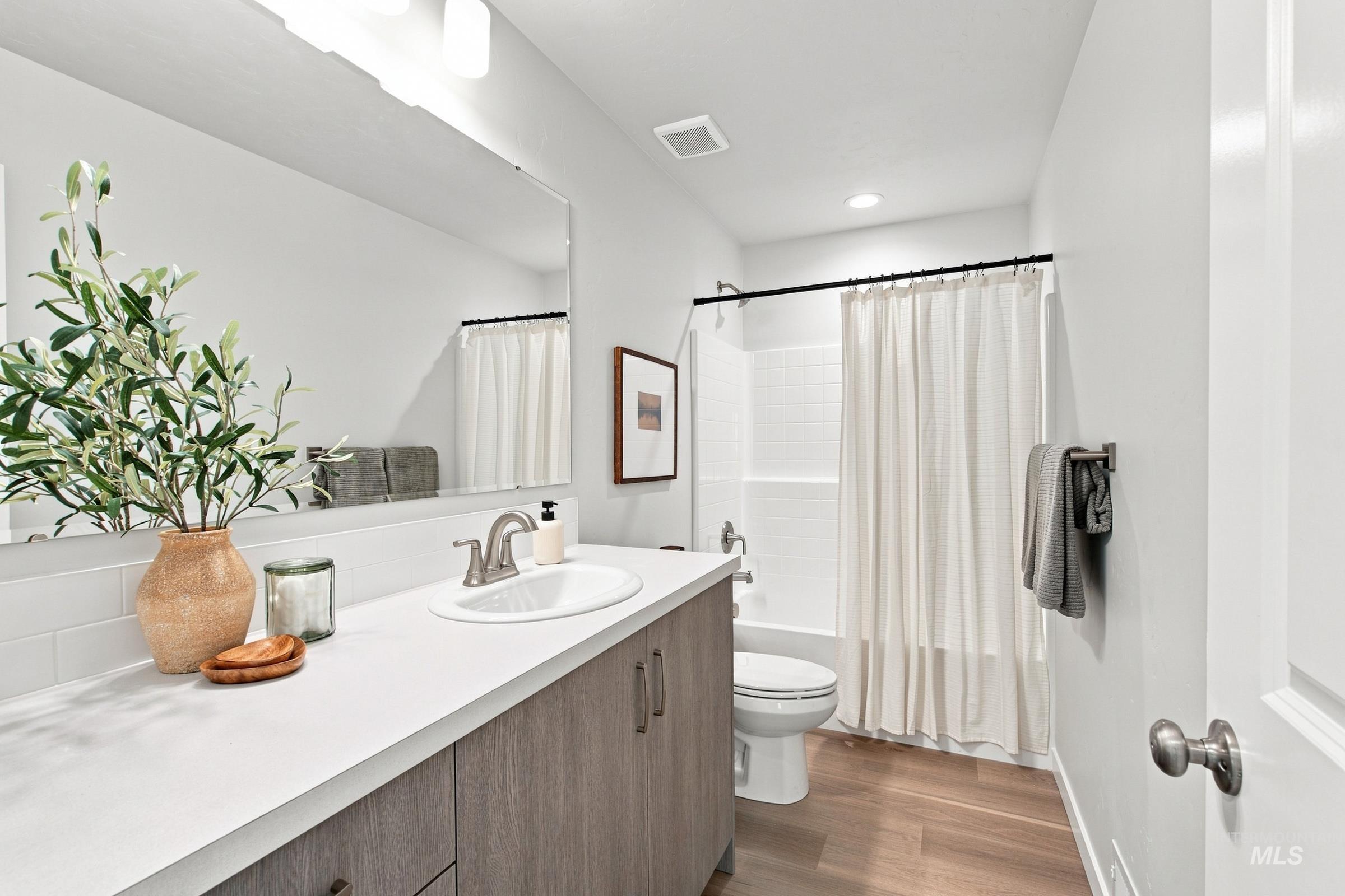 14044 Shiny Spruce Street Caldwell, ID 83607 - Photo 37 of 37 Wood-finish flooring, white subway tile backsplash, white countertop, wood-finish vanity with integrated sink, and white shower tile