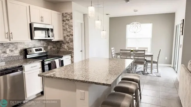 a kitchen with kitchen island granite countertop a table chairs sink and cabinets