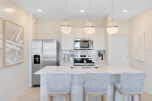 a kitchen with stainless steel appliances a refrigerator a stove a sink a dining table and chairs with wooden floor