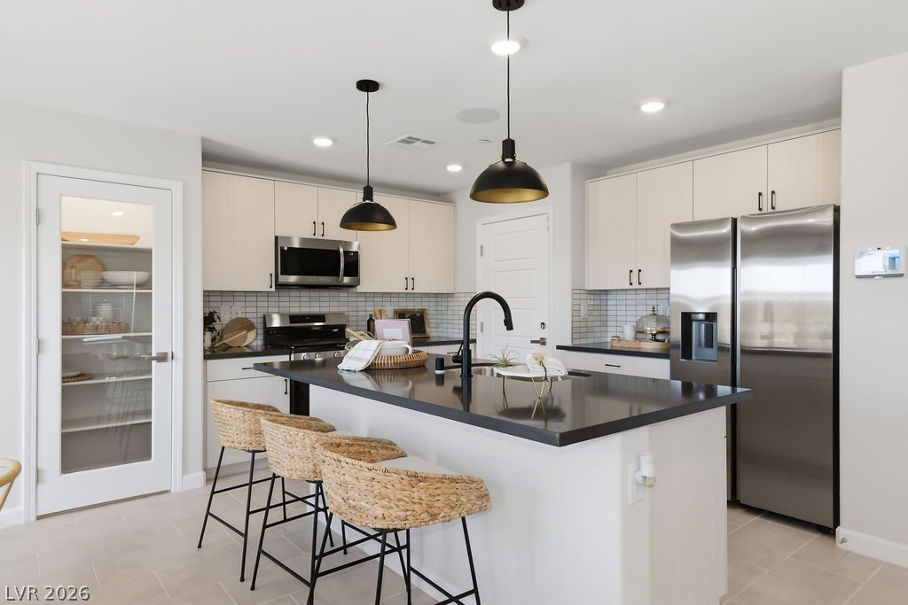 913 Cadence View Way Henderson, NV 89011 - Photo 18 of 46 A contemporary kitchen features an inviting island with dark countertops, complemented by sleek stainless steel appliances.