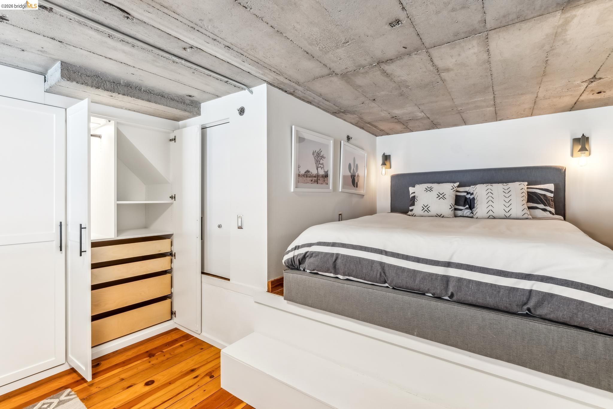255 3rd Street, Unit 206 Oakland, CA 94607 - Photo 5 of 7 Built-in cabinetry with multiple drawers and shelving, concrete ceiling, hardwood flooring, wall-mounted sconce lighting, and a raised platform