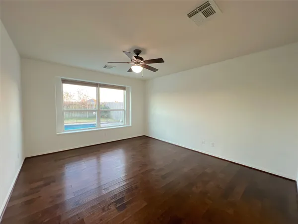 an empty room with wooden floor chandelier fan and windows
