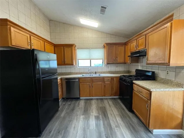 a kitchen with granite countertop a refrigerator stove top oven a sink and dishwasher with wooden floor