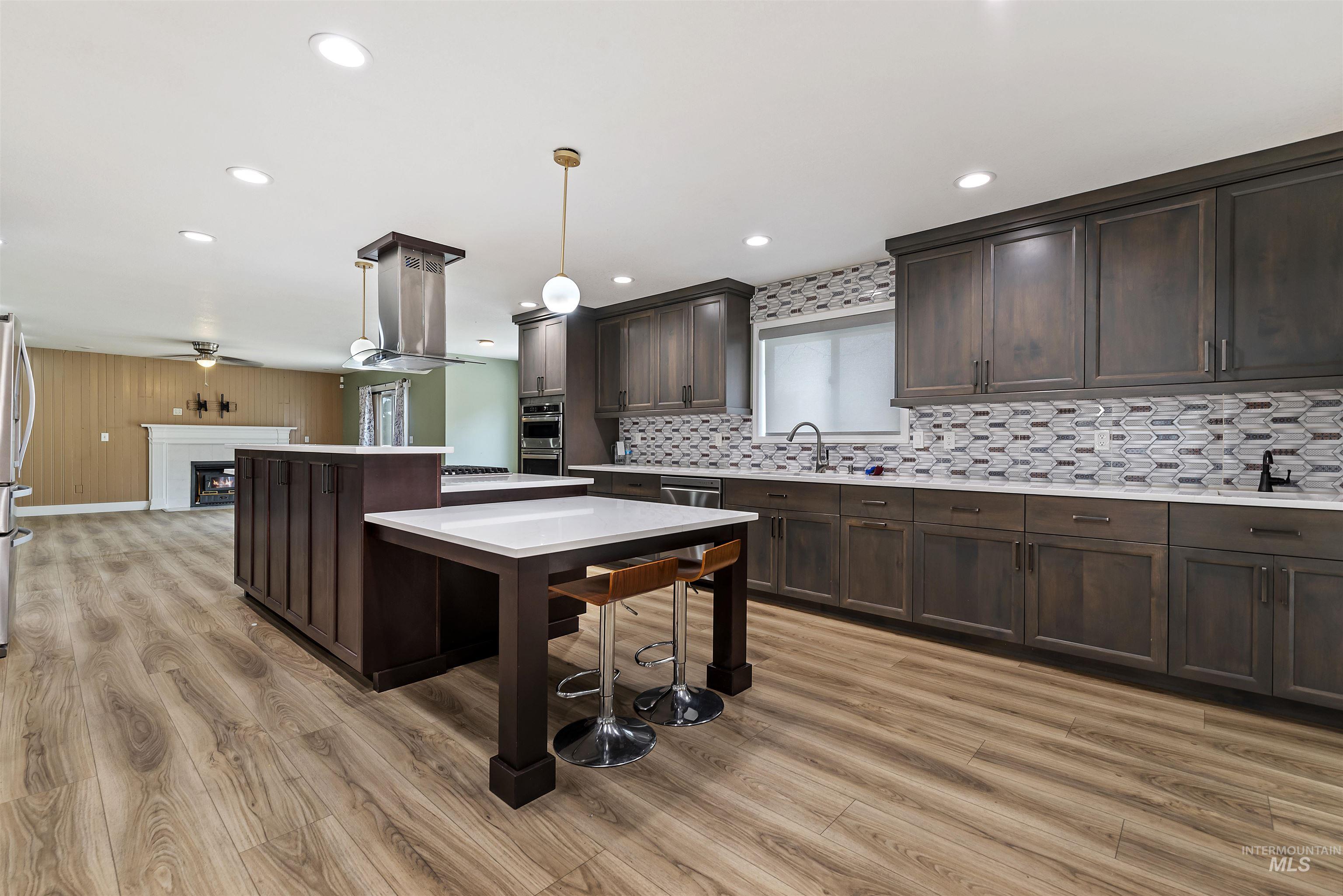 3160 East Springwood Drive Meridian, ID 83642 - Photo 14 of 41 Kitchen with dark brown cabinets, a fireplace, tasteful backsplash, hanging light fixtures, and a center island
