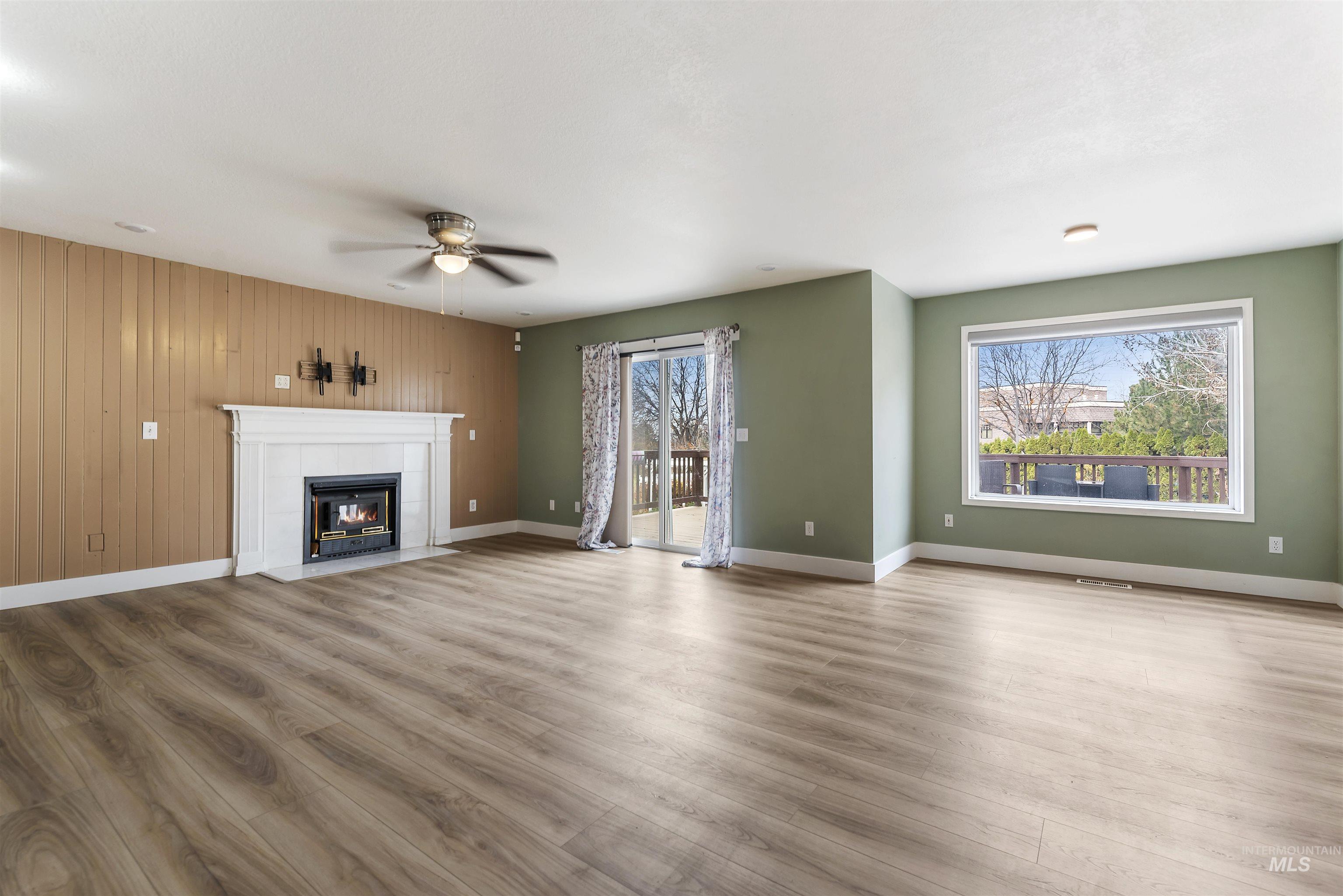3160 East Springwood Drive Meridian, ID 83642 - Photo 8 of 41 Unfurnished living room with a tiled fireplace, wood finished floors, wood walls, and a ceiling fan