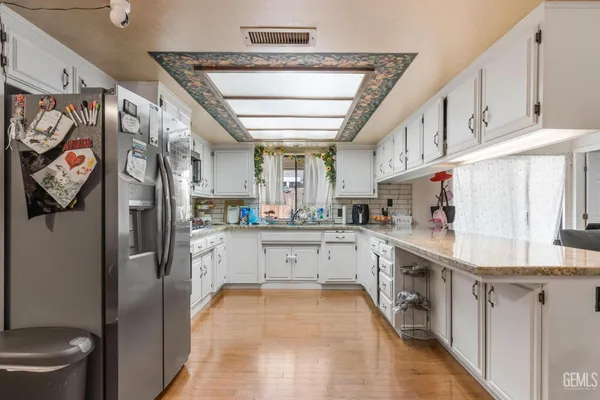 a kitchen with stainless steel appliances granite countertop a refrigerator a sink dishwasher a stove and white countertops with wooden floor