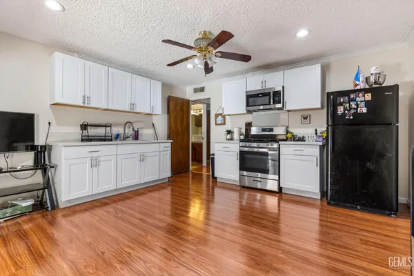 a kitchen with stainless steel appliances a refrigerator a sink dishwasher a stove and white cabinets with wooden floor