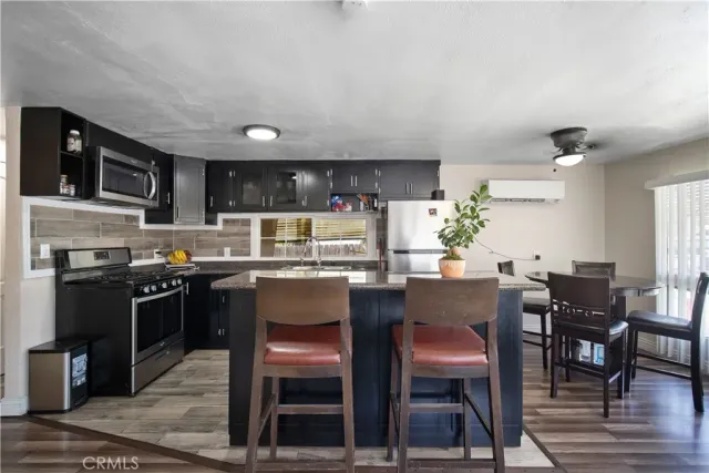 a kitchen with stainless steel appliances granite countertop a stove top oven a refrigerator a dining table and chairs with wooden floor