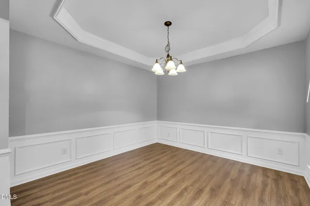 a view of an empty room with chandelier fan and wooden floor