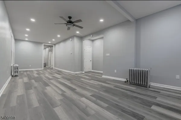 a view of an empty room with wooden floor and a ceiling fan