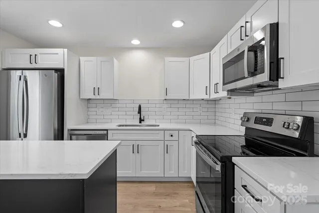 a kitchen with stainless steel appliances a sink a stove a microwave a refrigerator a sink and cabinets