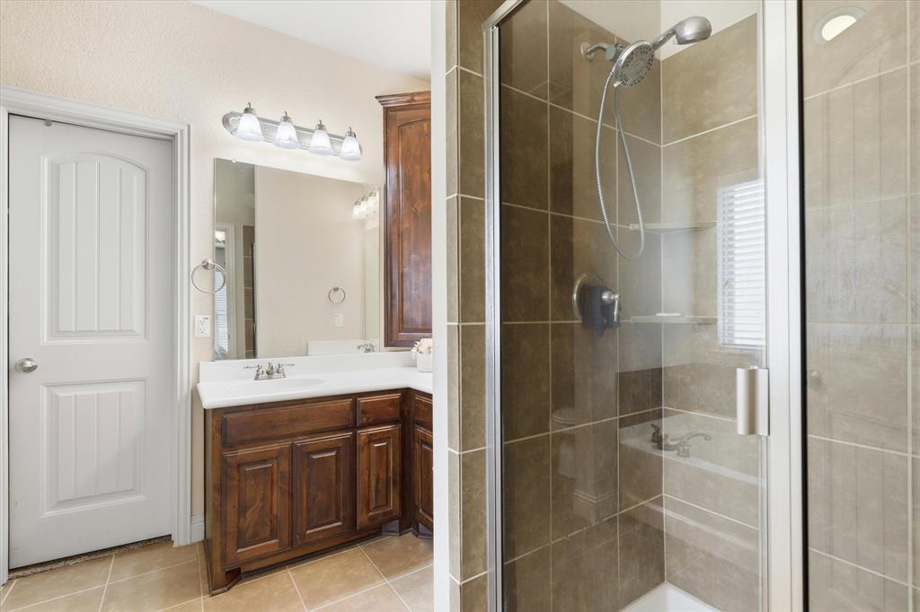 115 Blue Quail Road Red Oak, TX 75154 - Photo 14 of 35 Bathroom featuring a wood-finish vanity with a white countertop, a framed mirror, and a glass-enclosed shower with tiled walls and a built-in shelf