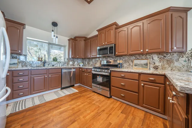 a kitchen with stainless steel appliances granite countertop wooden cabinets a dining table and chairs