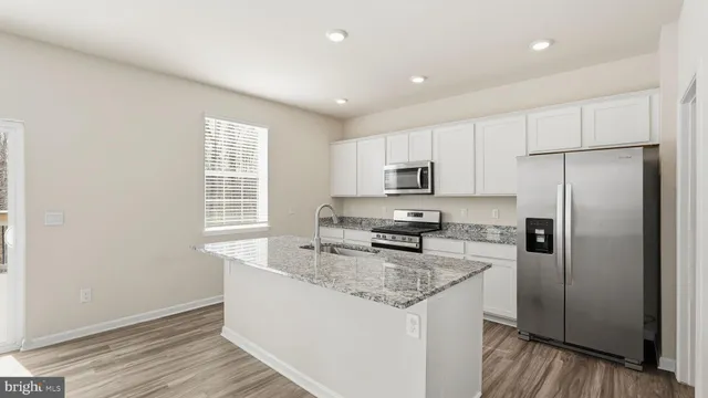 a kitchen with stainless steel appliances granite countertop a refrigerator a sink a stove a microwave and island with wooden floor