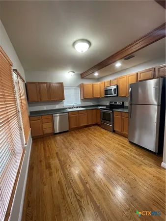 a kitchen with stainless steel appliances a refrigerator a sink dishwasher with a dining table and wooden floor
