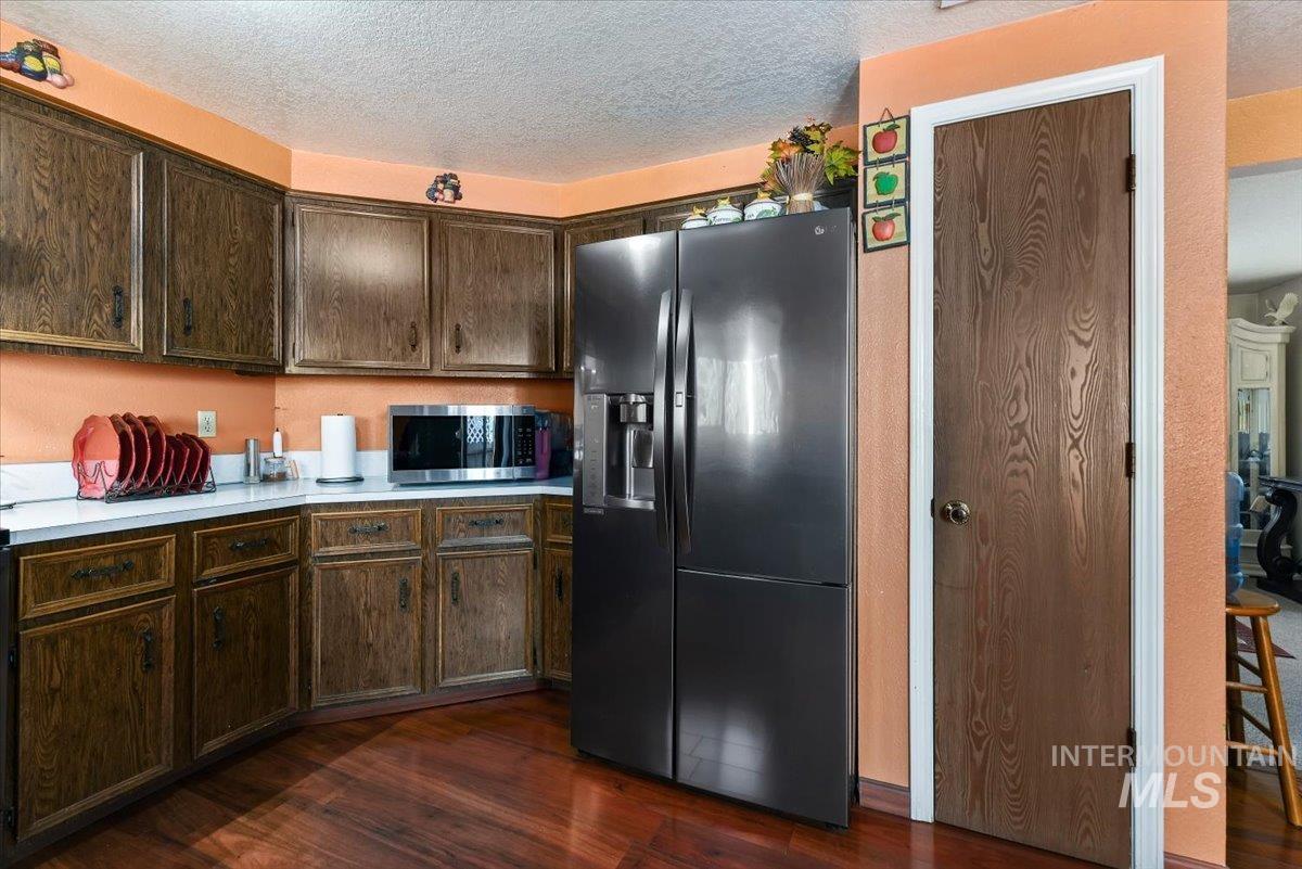 2811 Apollo Place Caldwell, ID 83605 - Photo 11 of 31 Kitchen with dark wood finish cabinets, light countertops, fridge with ice dispenser, dark wood-style flooring, and a textured ceiling