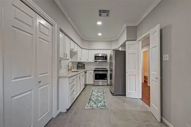 a large white kitchen with cabinets a sink and stainless steel appliances
