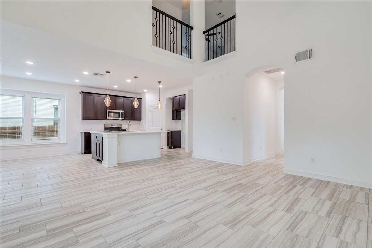 8008 Prairie Rye Drive Lago Vista, TX 78645 - Photo 20 of 40 Bright open-concept living space featuring wood-look tile flooring, a kitchen island with pendant lighting, dark wood cabinetry, stainless steel appliances, and an arched entryway