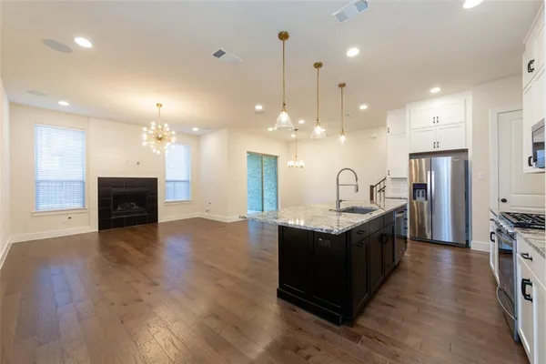 a kitchen with stainless steel appliances granite countertop a sink a stove a refrigerator and a fireplace with wooden floor
