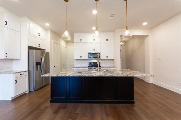 a kitchen with stainless steel appliances granite countertop a sink a refrigerator a center island and wooden floor