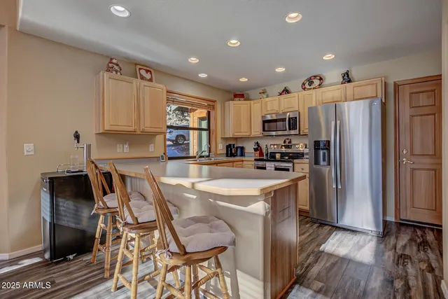 a kitchen with stainless steel appliances a refrigerator a stove a sink a dining table and chairs with wooden floor