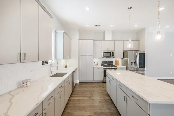 a large white kitchen with stainless steel appliances kitchen island granite countertop a sink a stove and a refrigerator