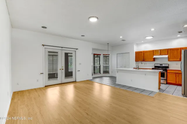 a view of an empty room with wooden floor and a kitchen