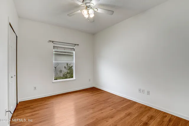 an empty room with wooden floor chandelier fan and windows