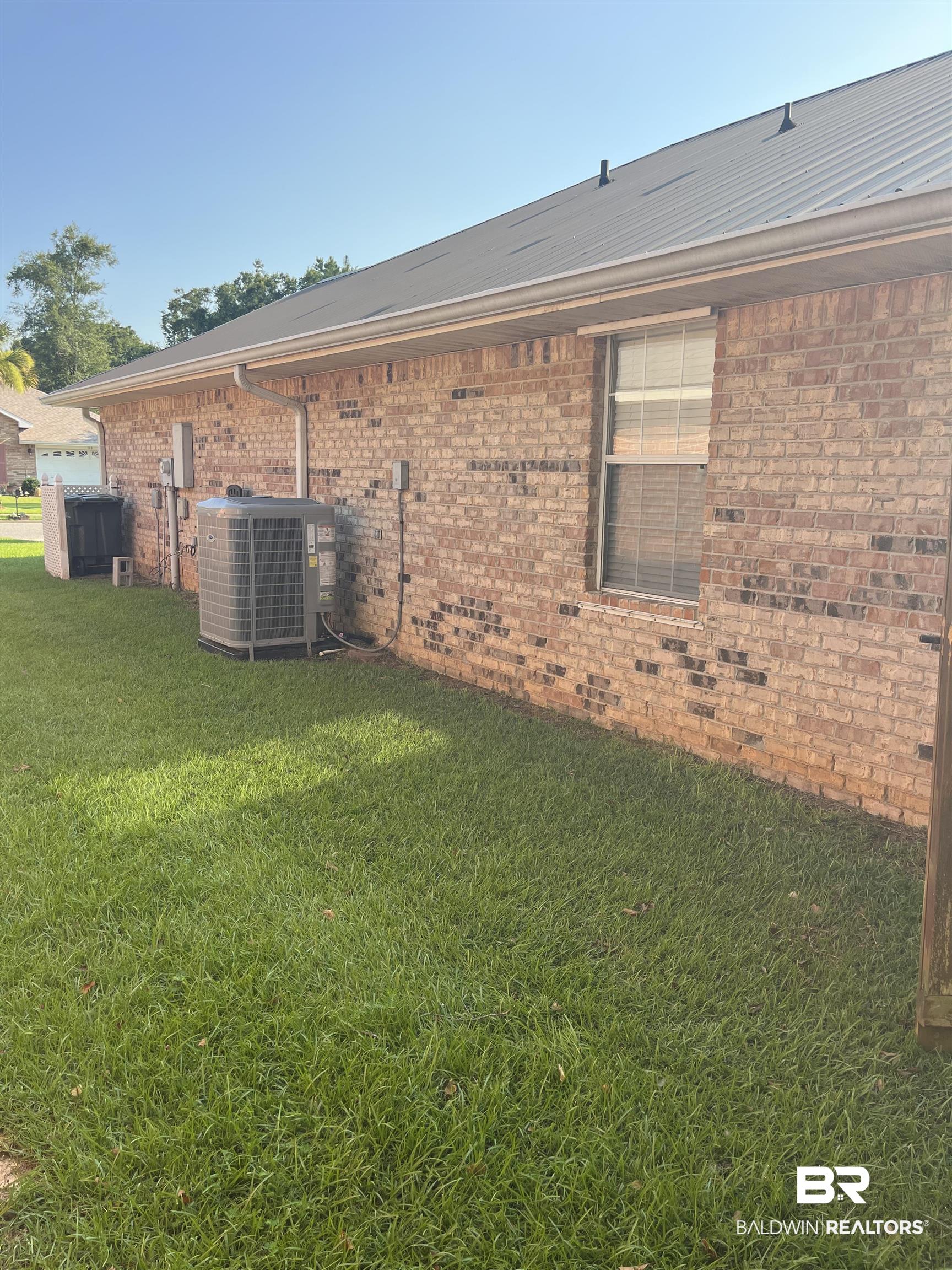 309 Cluster Street Foley, AL 36535 - Photo 31 of 38 Brick exterior featuring a metal roof, white rain gutters, and a single-pane window with blinds