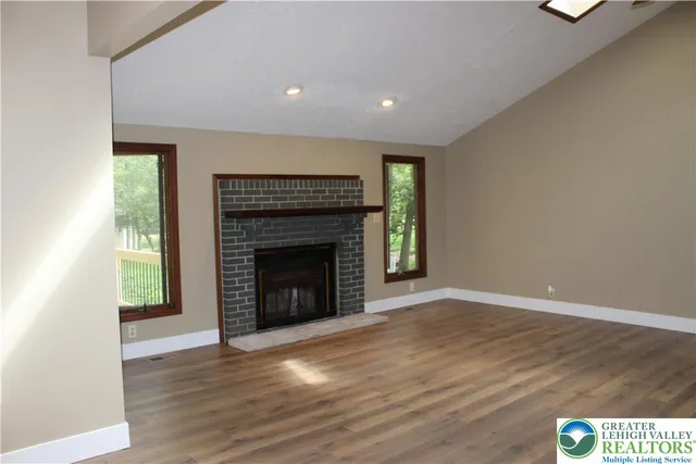 a view of an empty room with wooden floor fireplace and a window