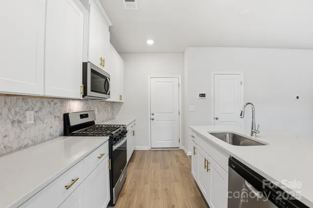 a kitchen with granite countertop a sink dishwasher stove and white cabinets with wooden floor