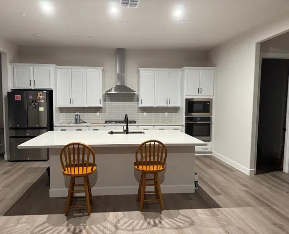 a kitchen with stainless steel appliances a dining table chairs refrigerator and sink