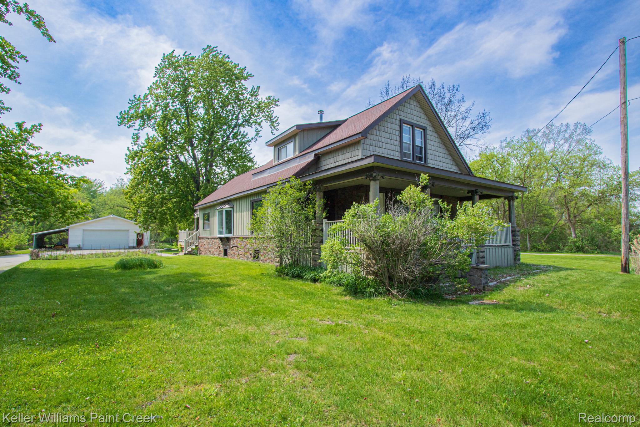View of side of property featuring a garage, a lawn, an outbuilding, and covered porch