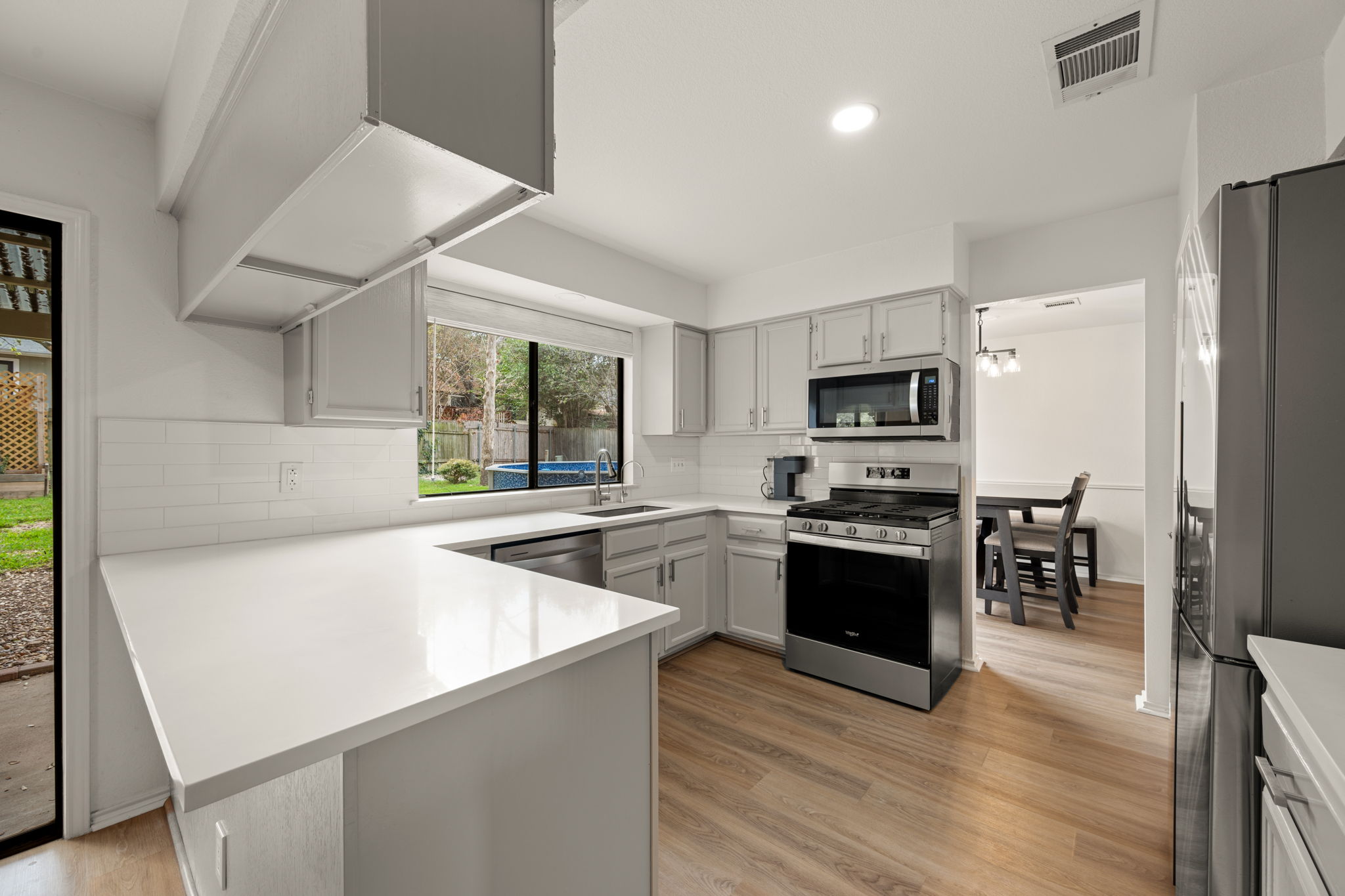 11942 Bittern Hollow Austin, TX 78758 - Photo 3 of 29 a kitchen with stainless steel appliances a stove top oven a sink dishwasher a refrigerator and a dining table with wooden floor