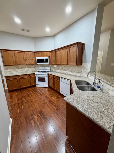 708 Ranier Lane Round Rock, TX 78665 - Photo 6 of 20 Kitchen featuring brown cabinetry, white appliances, light stone countertops, dark wood-style flooring, and tasteful backsplash